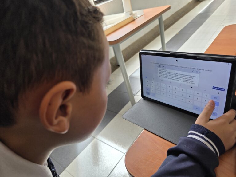 Estudiante redacta una historia en la tablet apoyado en una mesa del aula