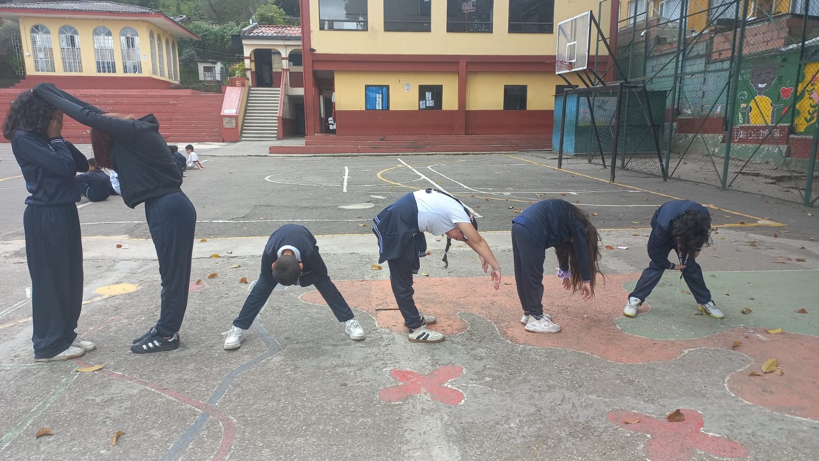 Estudiantes inclinan su cuerpo en el patio del colegio para formar letras en equipo