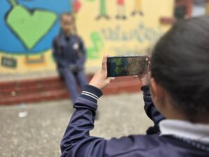 Estudiante encuadra con el celular una escena frente al mural de colores del colegio