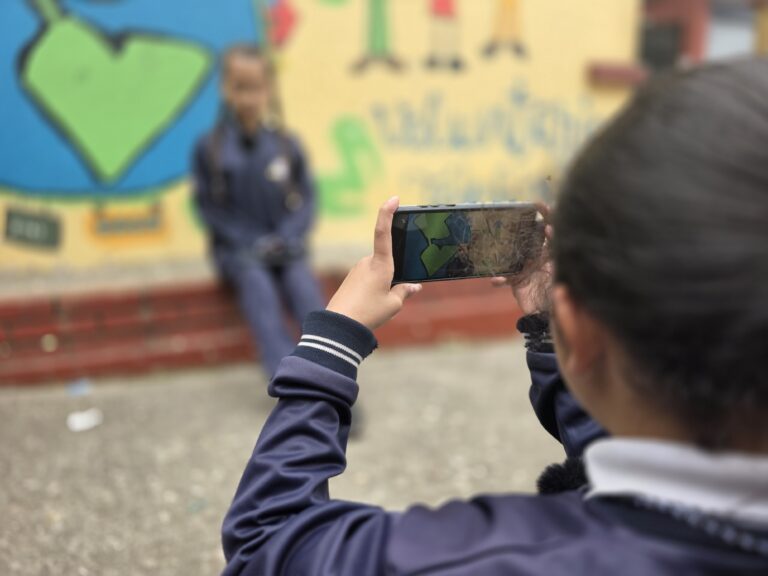 Estudiante encuadra con el celular una escena frente al mural de colores del colegio