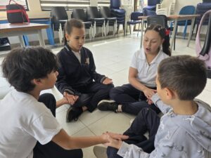Cuatro estudiantes sentados en círculo en el piso extienden las manos hacia el centro
