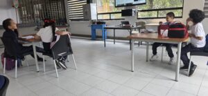Estudiantes sentados en las mesas del salón siguen la presentación proyectada en la pantalla