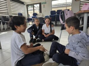 Estudiantes sentados en el piso conversan y acuerdan las reglas del juego en el aula múltiple