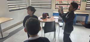 Estudiante sostiene la tablet con las dos manos para grabar a un compañero durante la práctica de entrevista