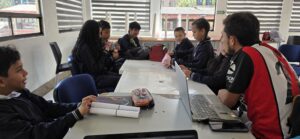 Vista general del salón del taller con estudiantes trabajando en mesas con cuadernos y equipos