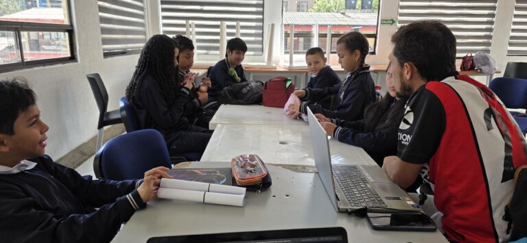 Vista general del salón del taller con estudiantes trabajando en mesas con cuadernos y equipos