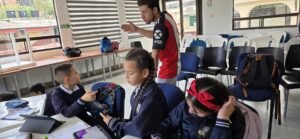 El docente acompaña a un grupo de estudiantes que trabaja con tablets en las mesas del salón