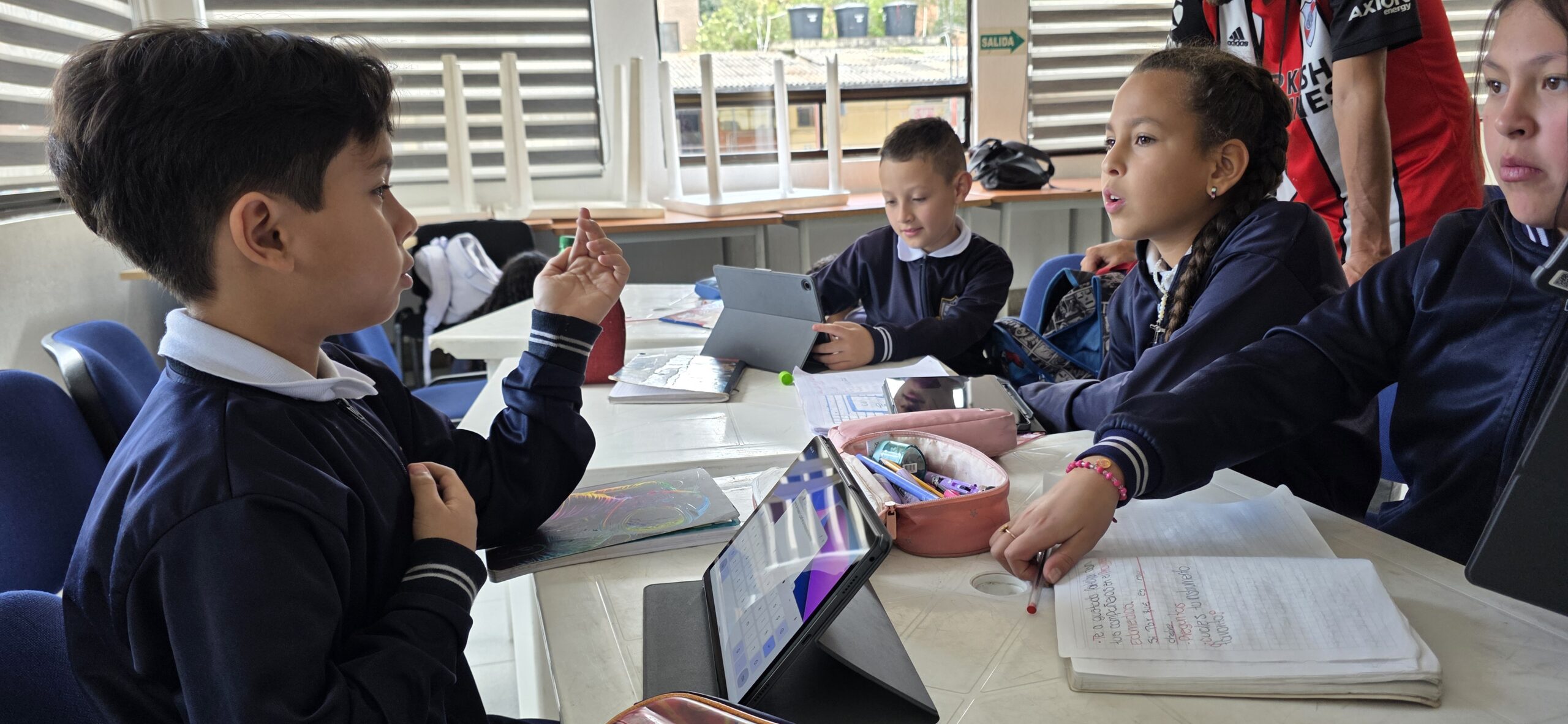 Un estudiante levanta la mano durante la sesión del taller mientras sus compañeros trabajan con tablets