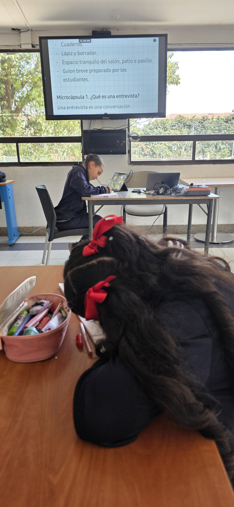 Detalle de la diapositiva con la definición de entrevista y una estudiante escribiendo su guion