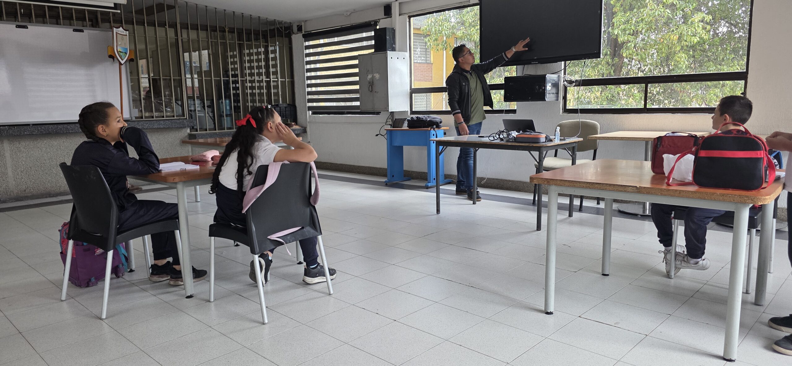 Vista general del aula: el docente conduce la sesión ante la pantalla mientras los estudiantes trabajan en sus mesas