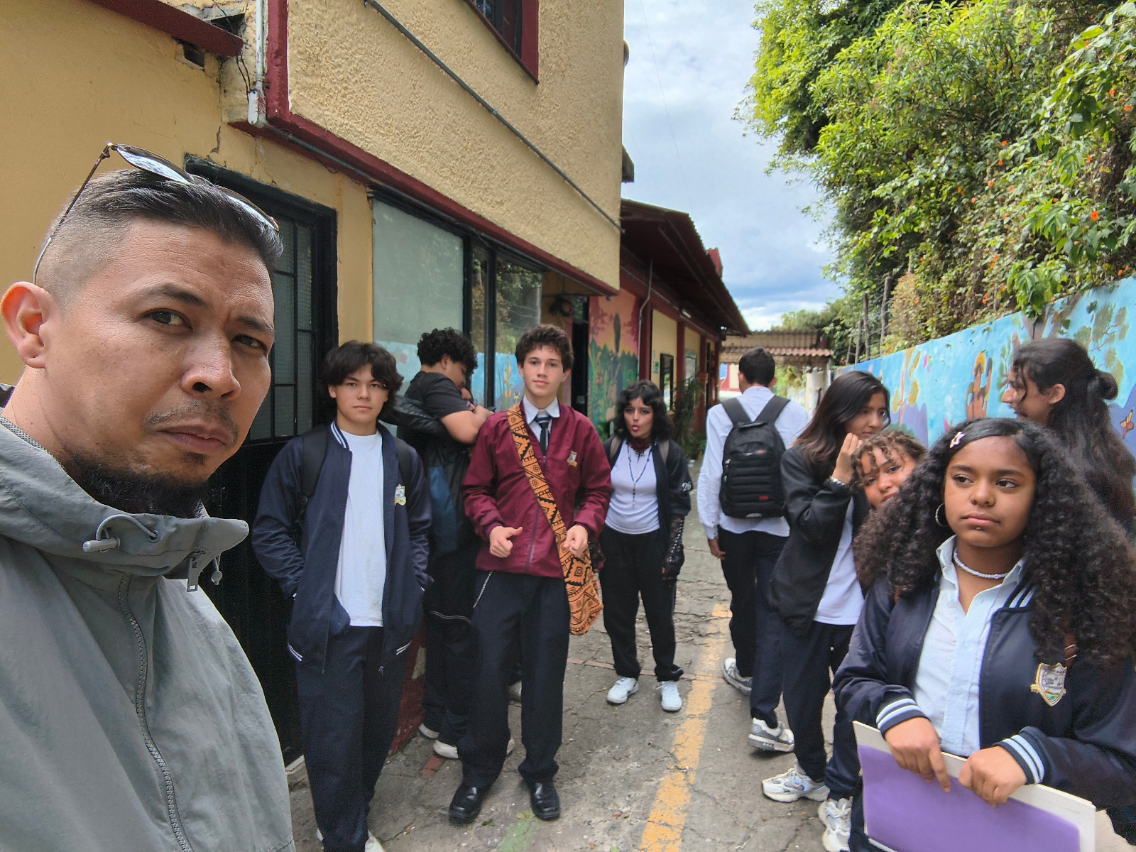 Grupo de estudiantes camina por el andén junto a un muro pintado durante una salida del taller, acompañados por su docente